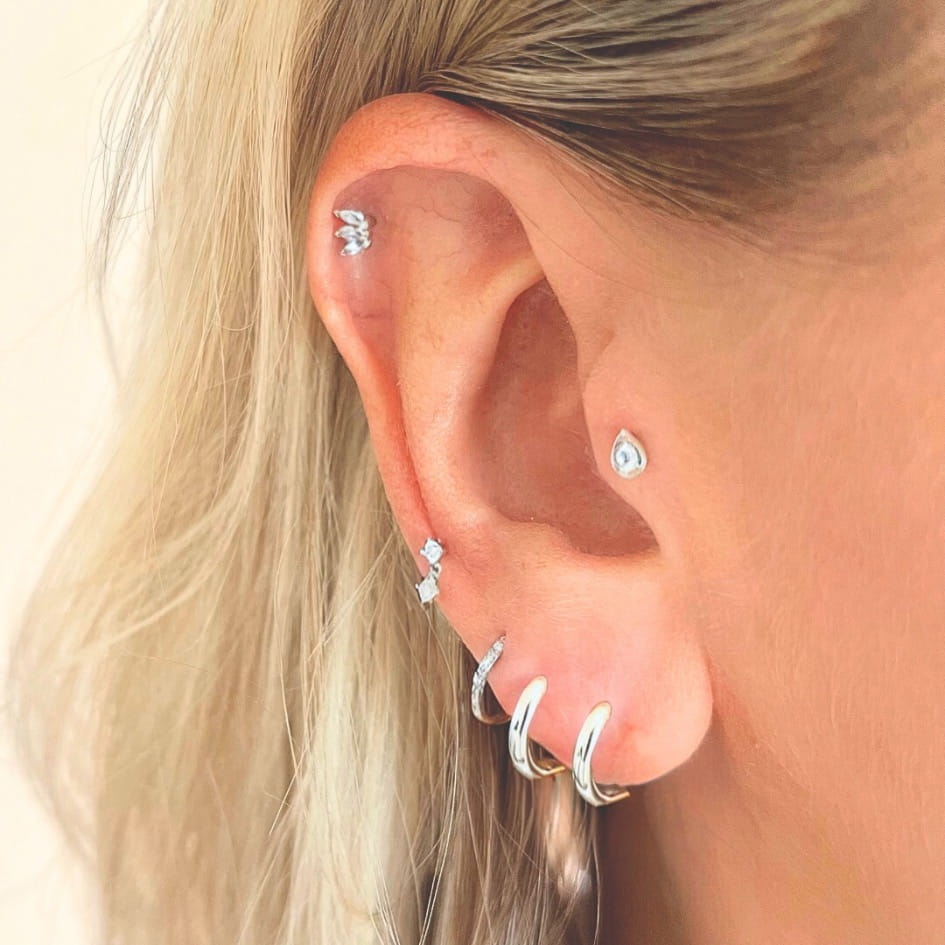 Close-up of an ear with multiple silver earrings on a neutral background
