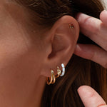 Close-up of an ear with gold hoop earrings and a hand adjusting hair.