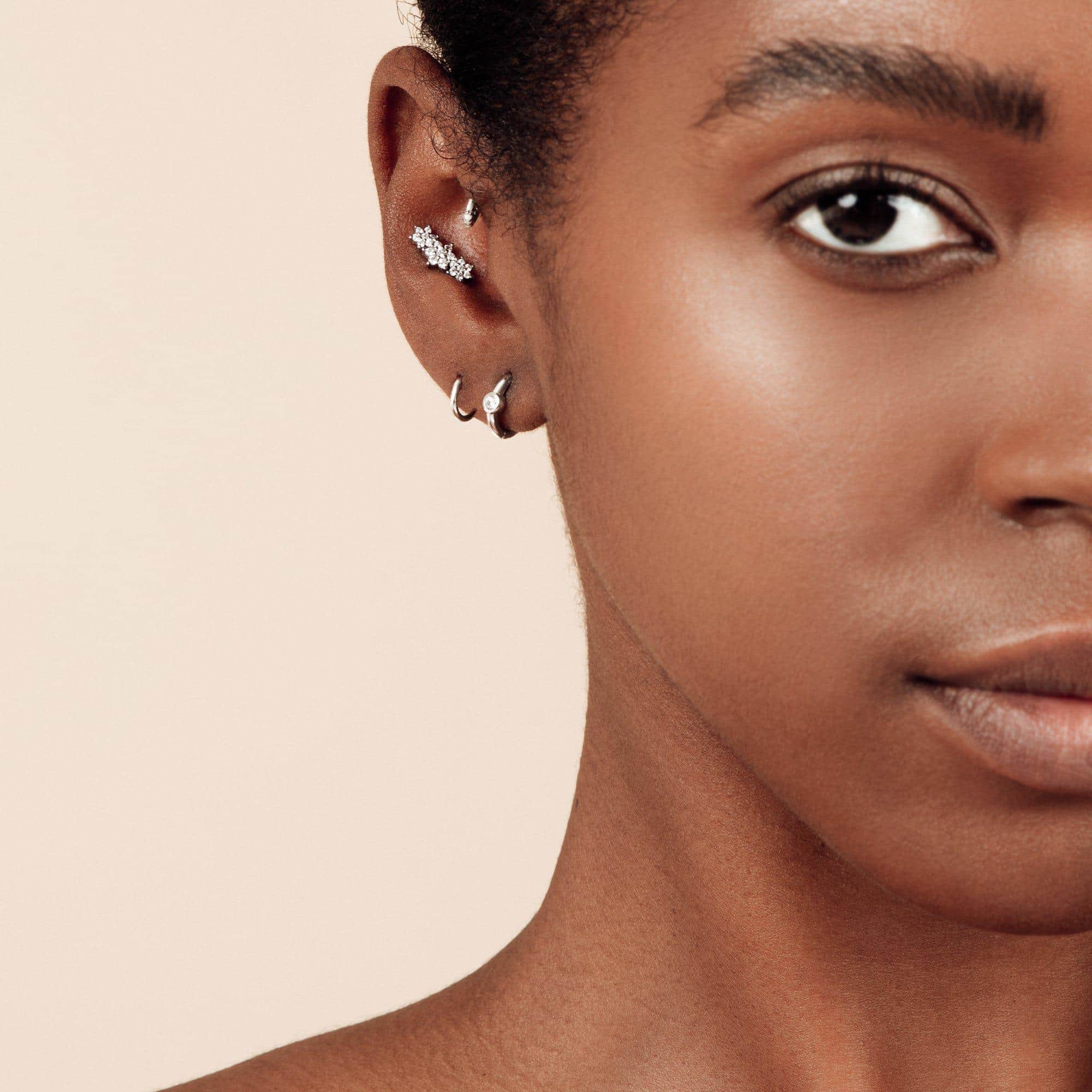 Close-up of a woman's ear wearing multiple earrings against a light background
