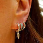 Close-up of an ear with gold and turquoise earrings.