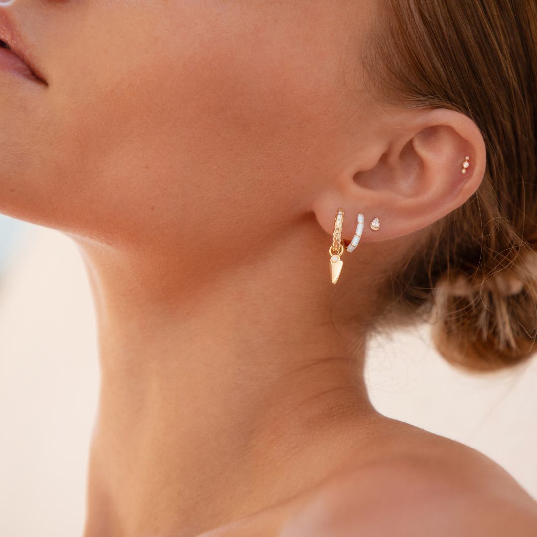 Close-up of a woman's ear wearing gold, opal and blue enamel earrings against a neutral background