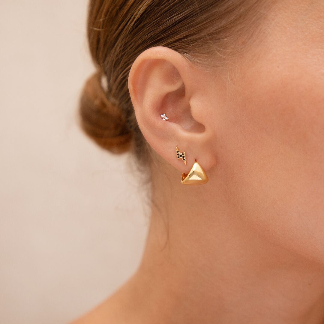Close-up of a person wearing gold triangle earrings with a neutral background