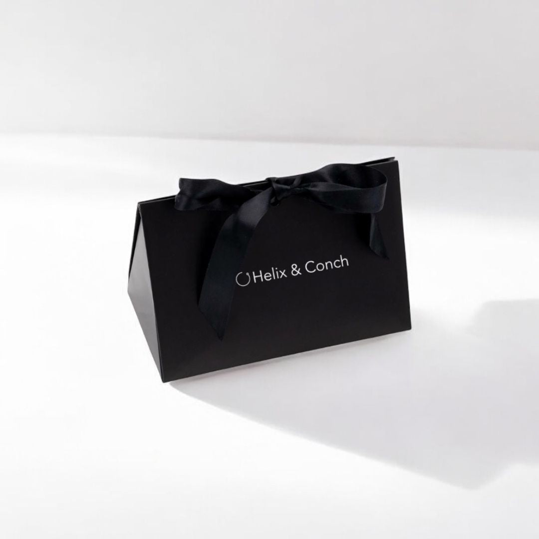 A black gift bag with 'helix & conch' branding, tied with a satin ribbon.