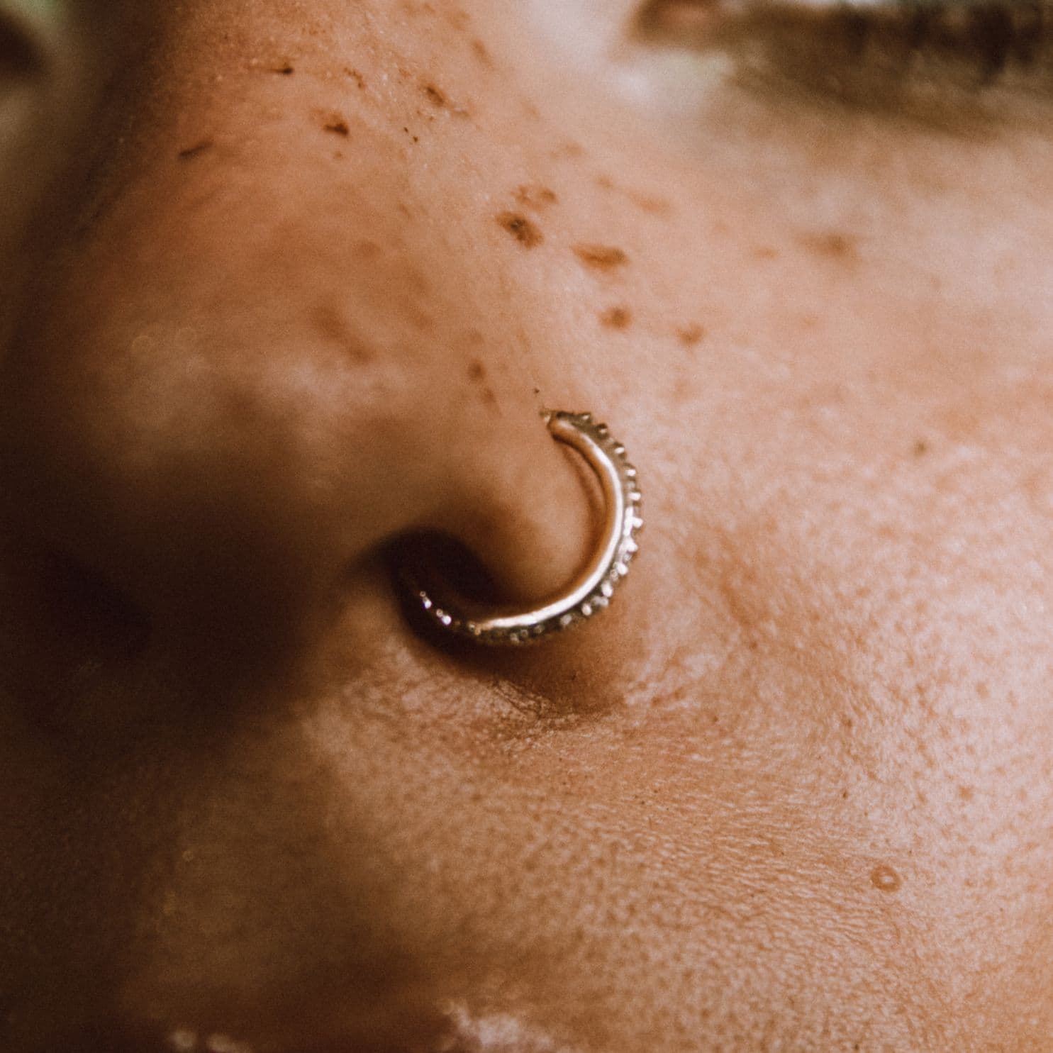 Close-up of a gold nose ring on a person's nose.