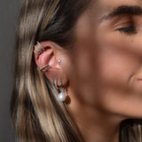 Close-up of a woman's ear with multiple earrings against a neutral background