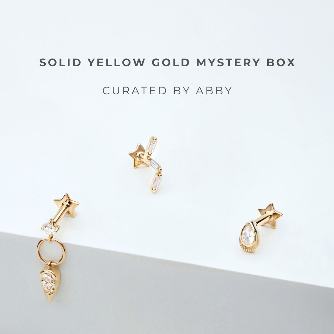 Solid yellow gold earrings on a light gray background with text 'Solid Yellow Gold Mystery Box Curated by Abby'.