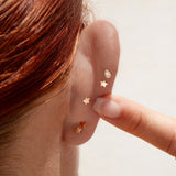 Close-up of a person wearing gold star-shaped earrings on a neutral background