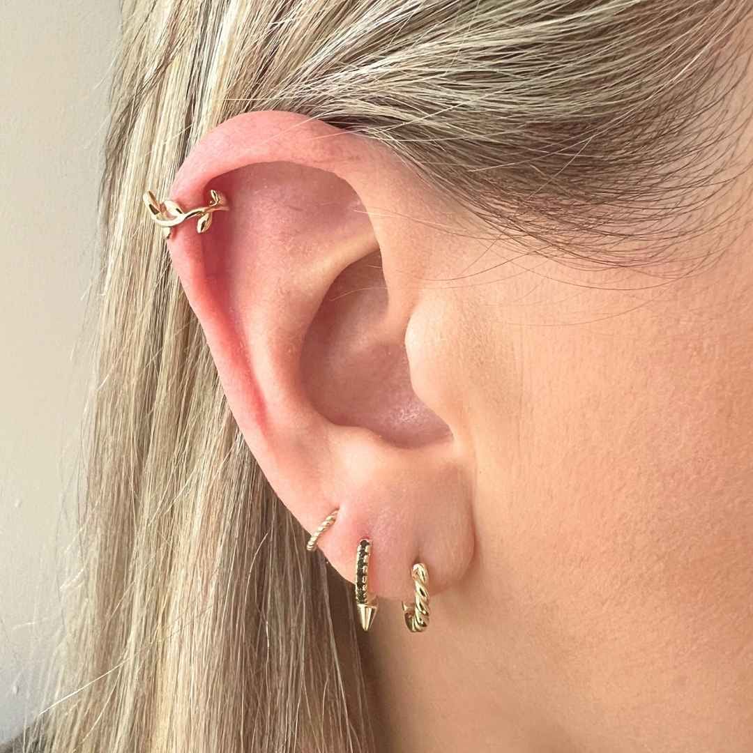 Close up of ear with vine hoop in helix piercing, and 3 gold earrings in the lobes
