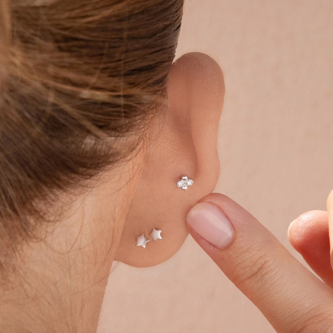 Close-up of a person wearing silver earrings on a beige background