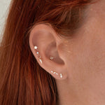 Close-up of an ear with multiple gold earrings against a neutral background