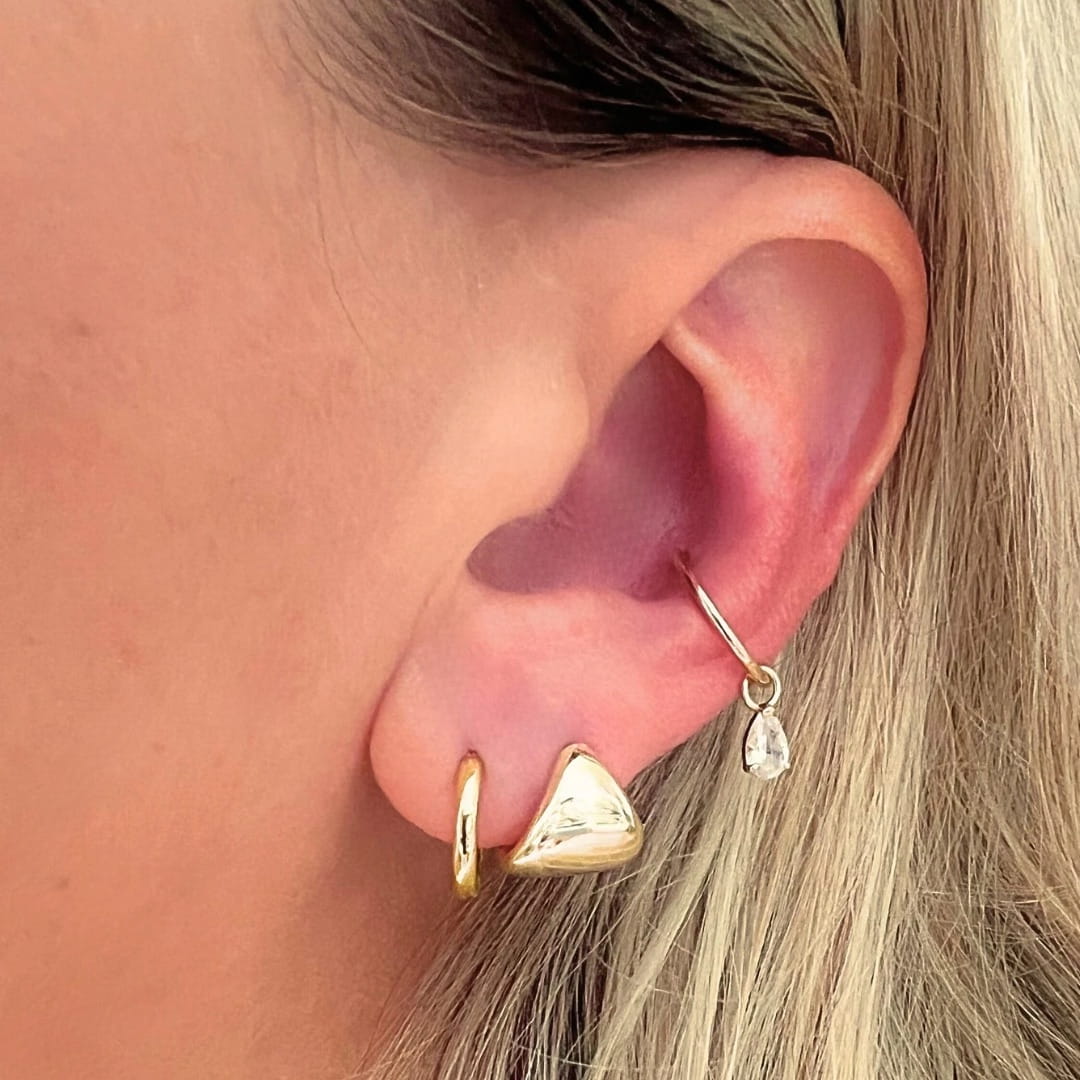 Close-up of an ear wearing gold earrings with a soft background