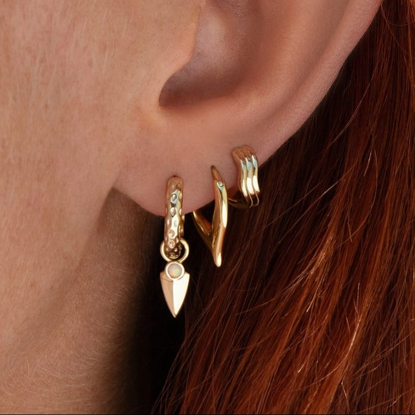 Close-up of an ear wearing gold hoop earrings with a red hair background