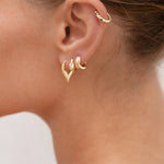 Close-up of a person's ear wearing gold hoop earrings with a blurred background