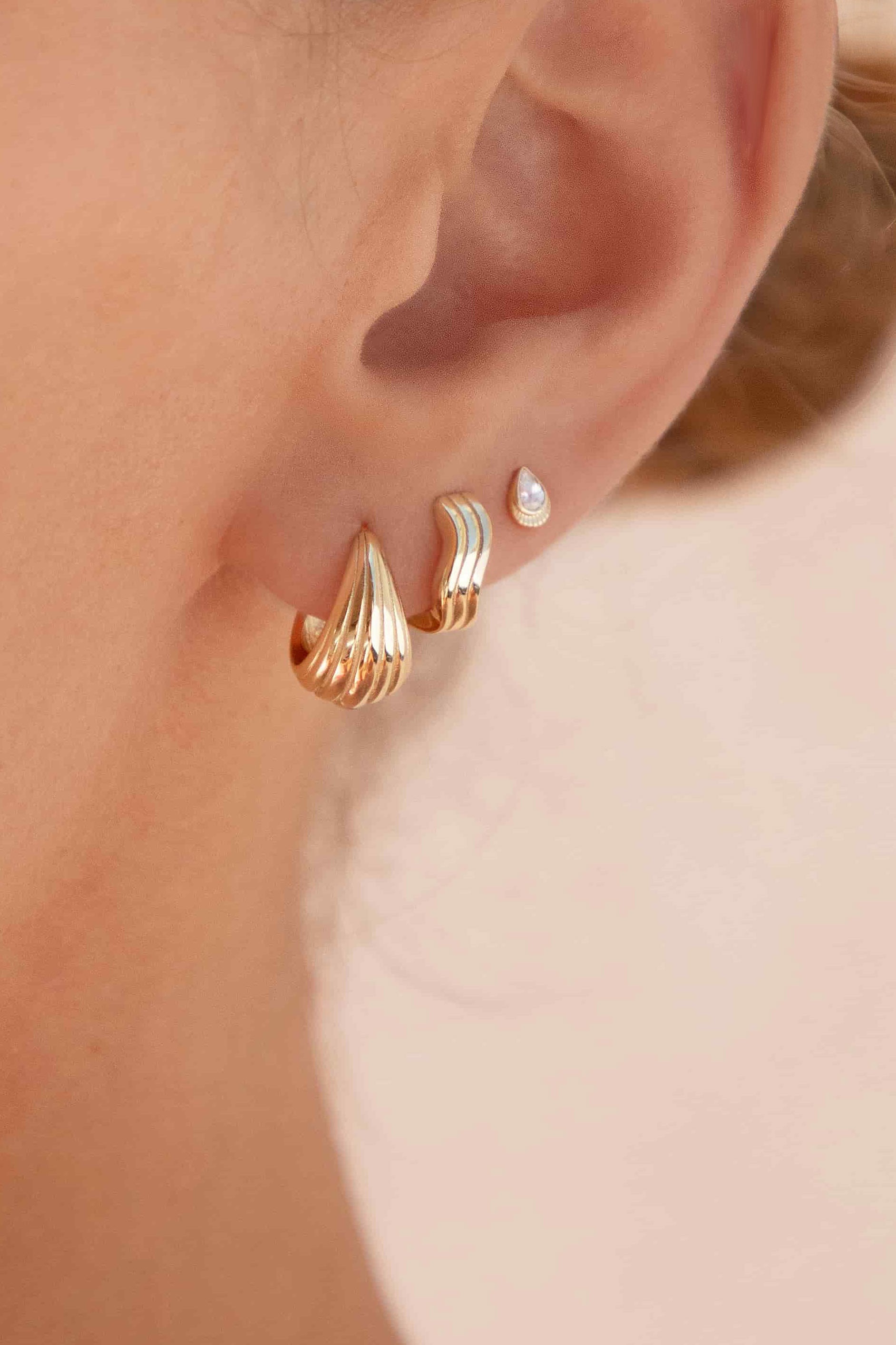 Close-up of an ear wearing gold hoop earrings with a blurred background