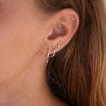 Close-up of an ear with multiple earrings against a neutral background